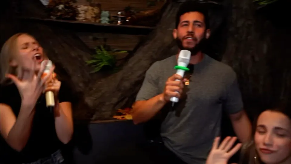A group of friends singing into a microphone in a private karaoke room at Secret Hangout in Orlando
